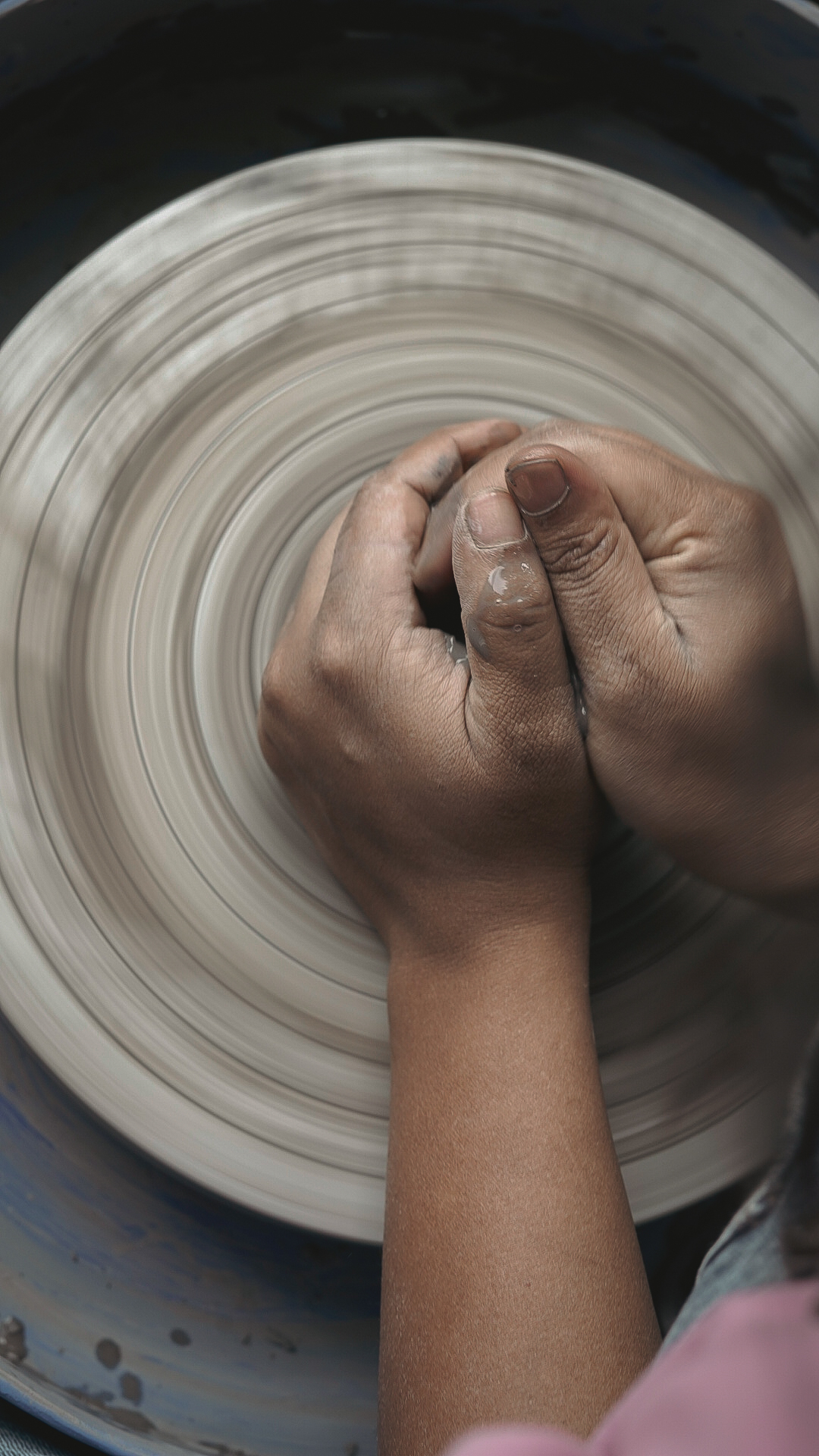 Hands centering wet clay on a spinning wheel